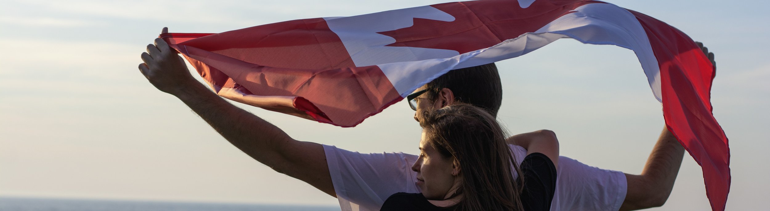 A couple stand in front of an ocean holding a Canadian flag