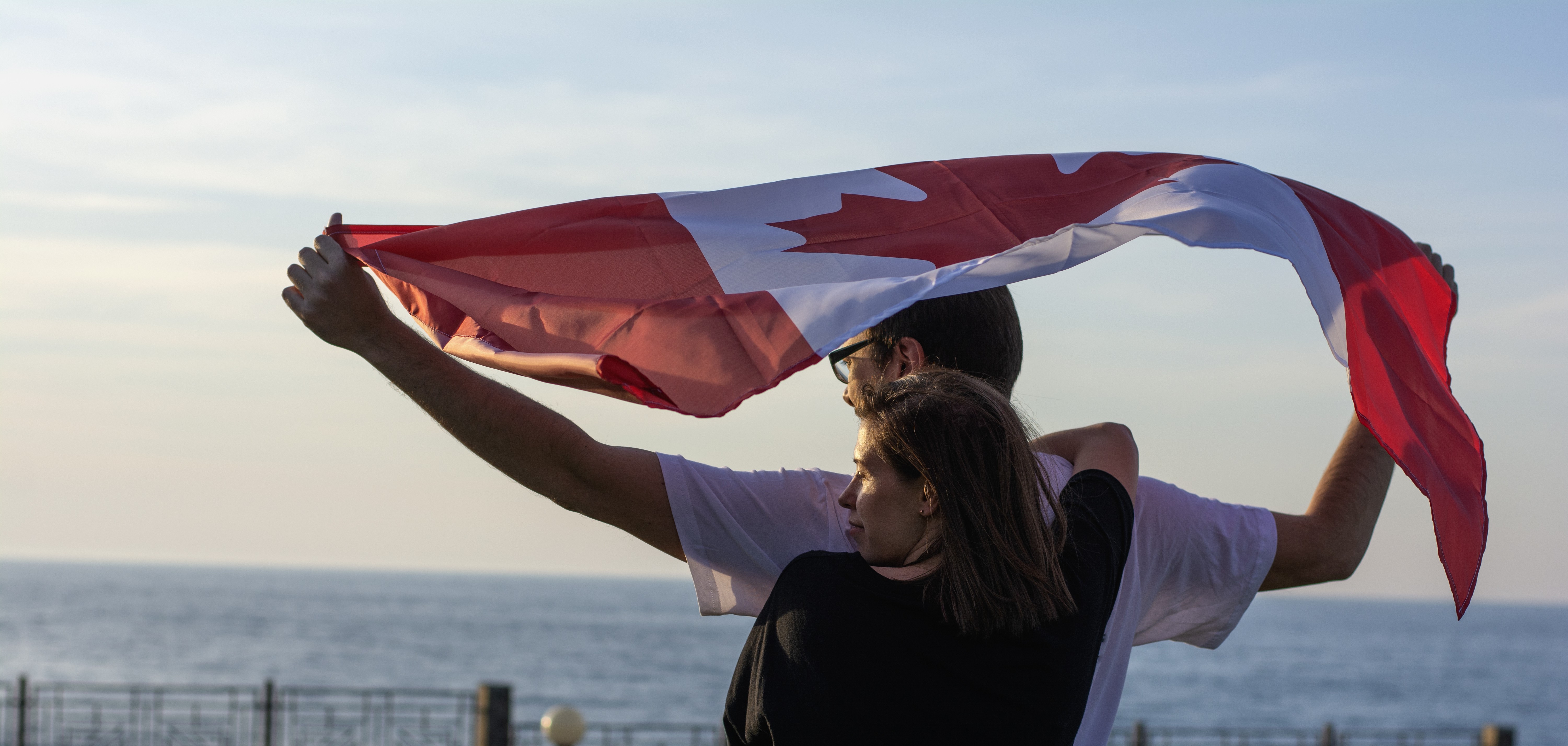 A couple stand in front of an ocean holding a Canadian flag